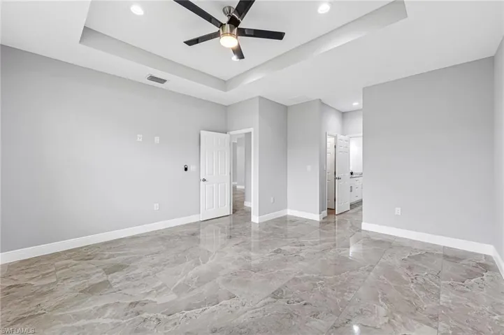 Unfurnished bedroom featuring ceiling fan, a raised ceiling, ensuite bathroom, and light tile floors