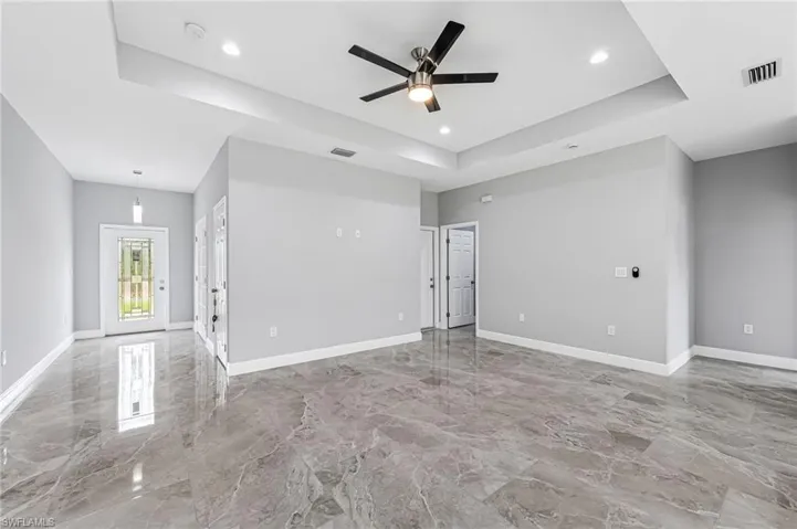 Empty room with a tray ceiling, tile flooring, and ceiling fan