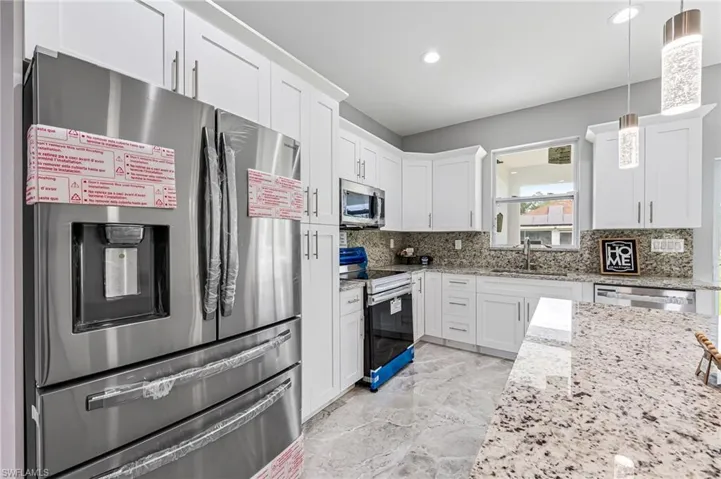 Kitchen featuring tasteful backsplash, stainless steel appliances, light tile floors, hanging light fixtures, and white cabinets