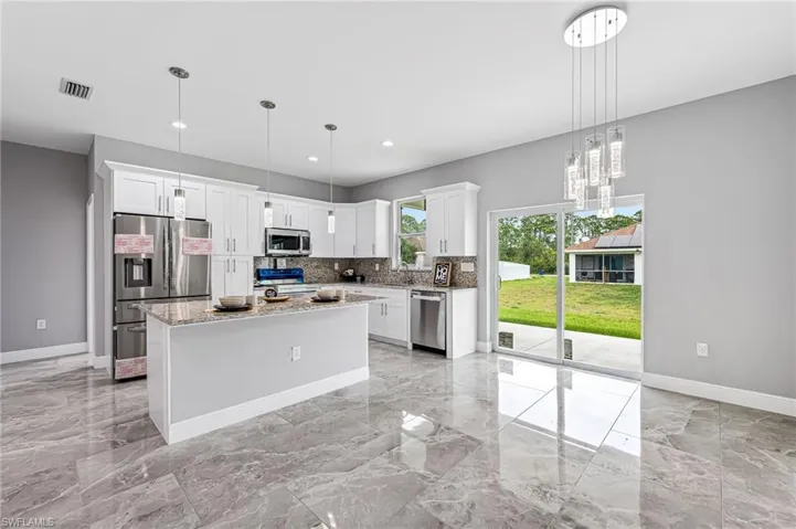 Kitchen with light stone counters, white cabinetry, a center island, appliances with stainless steel finishes, and pendant lighting