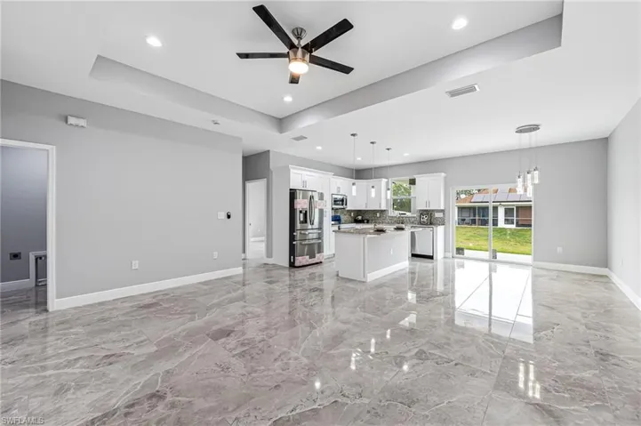 Unfurnished living room with ceiling fan, a tray ceiling, and light tile floors