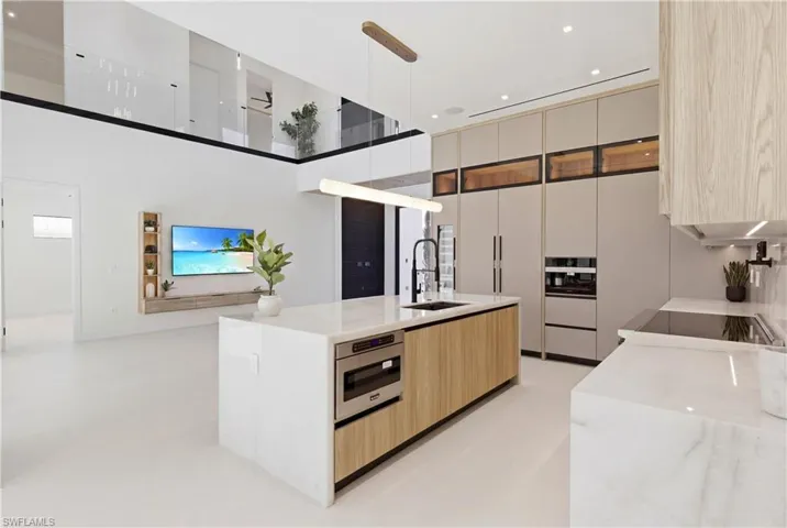 The oversized waterfall island serves as a stunning centerpiece, highlighted by a Cristallo quartzite lighting pendant, and complemented by top-of-the-line cabinetry extending to the ceiling with under- and upper-cabinet lighting, Cristallo quartzite countertops, full-height backsplash, pot filler, and a large sink with a designer spring single-handle faucet for elevated functionality and style.