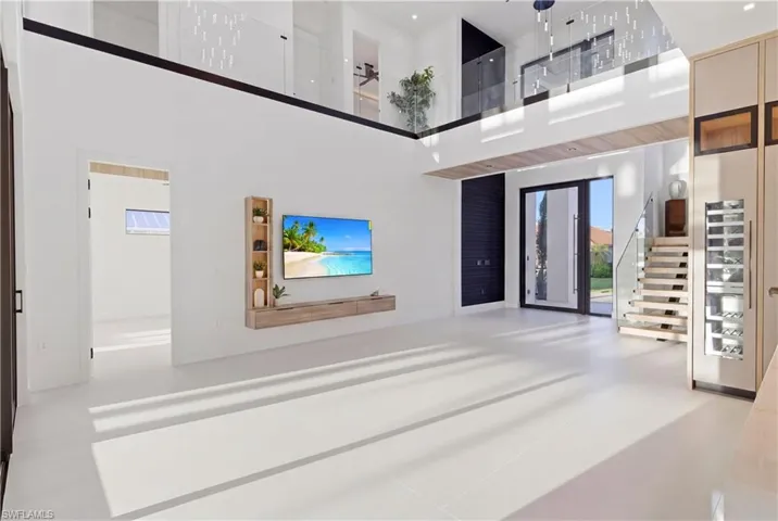 Living room showcasing custom wood beam detailing, Italian wallpapered feature wall with illuminated built-ins, and a stunning 64” multi-drop chandelier cascading from the ceiling, complemented by a 75” TV and premium Bose surround sound system for elevated modern living.