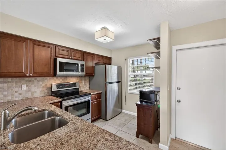 Kitchen featuring stainless steel appliances, light stone counters, backsplash, light tile patterned floors, and a textured ceiling