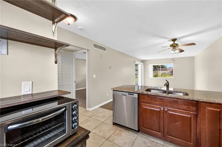 Kitchen featuring stainless steel dishwasher, a ceiling fan, light stone countertops, and light tile patterned flooring