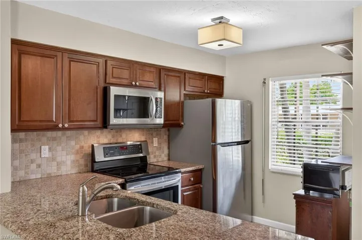 Kitchen with stainless steel appliances, tasteful backsplash, wood finish cabinets, and light stone counters