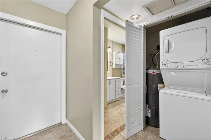 Laundry area with electric water heater, stacked washing machine and dryer, and light tile patterned floors