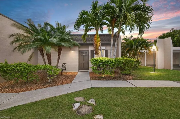 View of front of property featuring a front yard, brick siding, mansard roof, and stucco siding