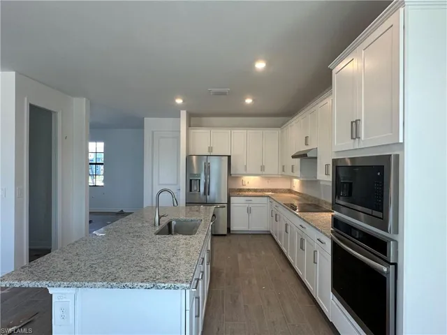 Kitchen featuring white cabinetry, wood-type flooring, a center island with sink, and stainless steel appliances