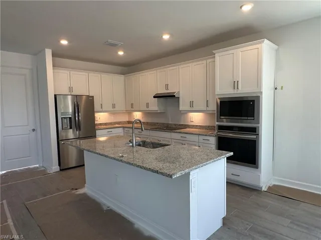 Kitchen with white cabinetry, a center island with sink, appliances with stainless steel finishes, hardwood / wood-style flooring, and sink
