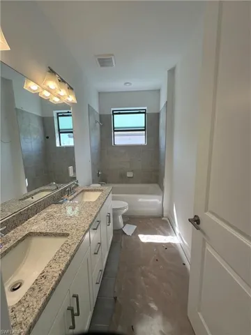 Full bathroom featuring tiled shower / bath, toilet, and dual bowl vanity