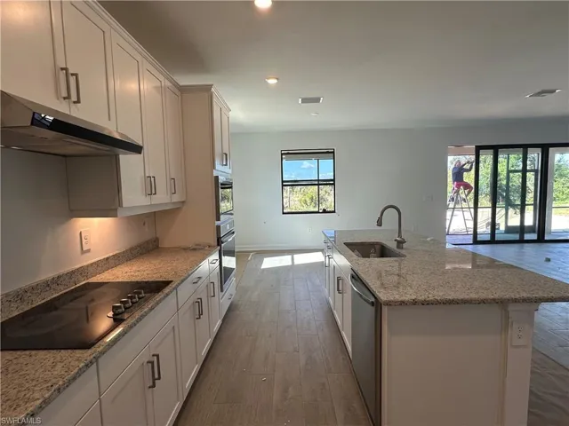 Kitchen with dark wood-type flooring, appliances with stainless steel finishes, white cabinets, a kitchen island with sink, and sink