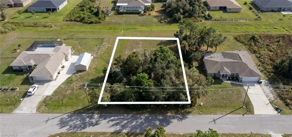 Vacant lot featuring established trees and a cleared area, positioned on a paved street