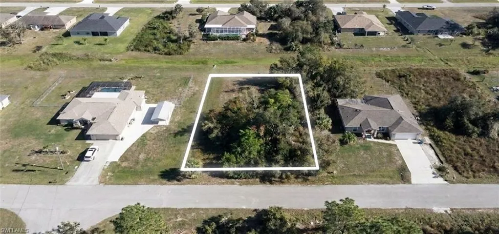 Cleared lot featuring a paved road frontage, natural vegetation, and surrounding residential properties