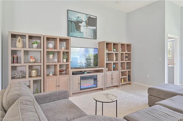 Living area with a glass covered fireplace, light tile patterned floors, and a high ceiling