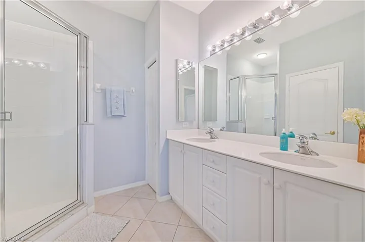 Full bath with a shower stall, double vanity, and light tile patterned floors