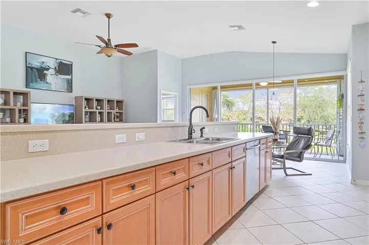 Kitchen featuring light wood finish cabinets, light tile patterned flooring, ceiling fan, pendant lighting, and lofted ceiling