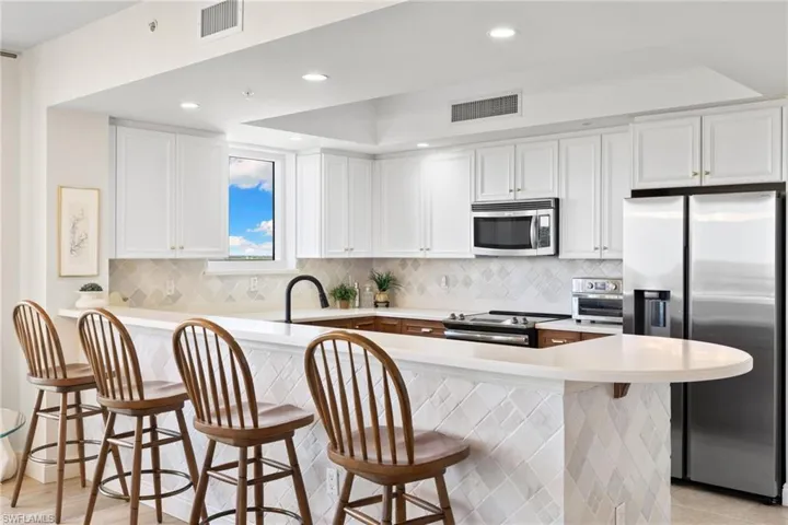 Kitchen with appliances with stainless steel finishes, white cabinets, a breakfast bar, recessed lighting, and decorative backsplash
