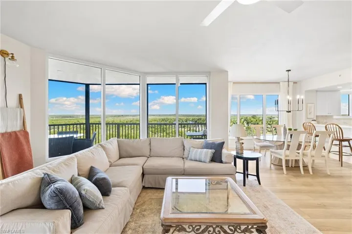 Living room with floor to ceiling windows, wood finished floors, a chandelier, and a ceiling fan