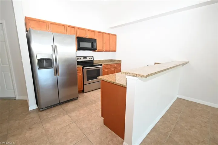Kitchen featuring stainless steel appliances, wood-finish cabinetry, a built-in microwave, and granite countertops