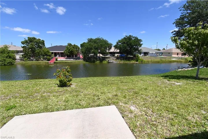 Expansive grassy area with a concrete slab, bordered by a calm body of water