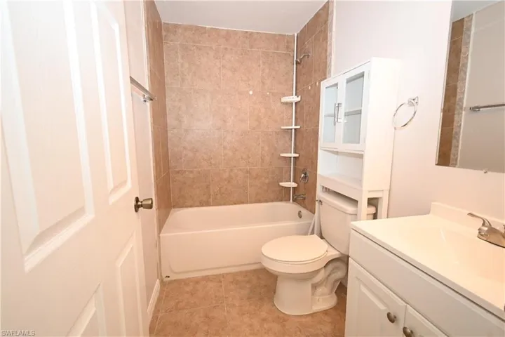 Bathroom featuring a white bathtub, ceramic tile shower surround, coordinating ceramic tile flooring, a white vanity with integrated sink, and an over-the-toilet storage cabinet