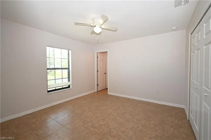 Spacious room featuring neutral wall tones, large window with grid panes, ceiling fan, tile flooring, and bi-fold closet doors
