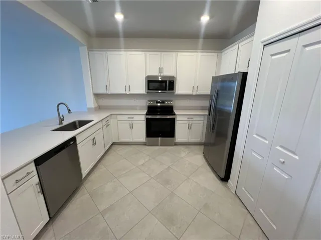 Kitchen featuring white cabinetry, light countertops, stainless steel appliances, a sink, and light tile patterned flooring
