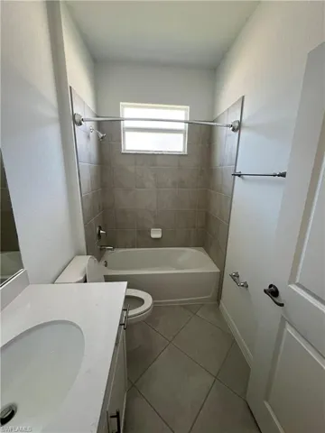 Full bath with washtub / shower combination, tile patterned floors, vanity, and toilet