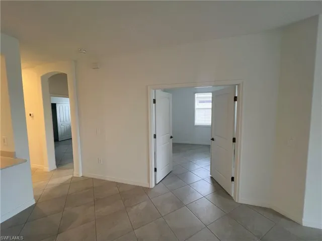 Empty room featuring tile patterned floors, arched walkways, and baseboards