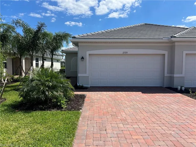 View of front facade with stucco siding, a tiled roof, decorative driveway, and an attached garage