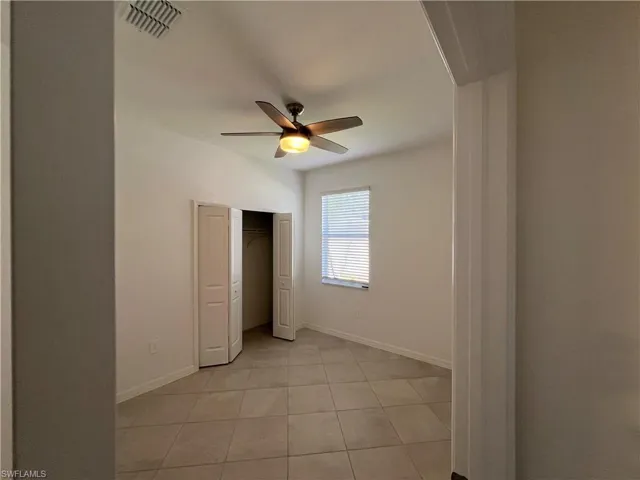 Unfurnished bedroom with light tile patterned floors, a closet, a ceiling fan, visible vents, and baseboards