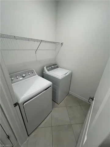Clothes washing area featuring light tile patterned flooring, baseboards, washer and dryer, and laundry area