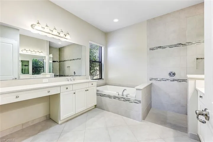 Primary Bathroom with two vanities, a garden tub, light tile patterned flooring, walk in shower, and recessed lighting