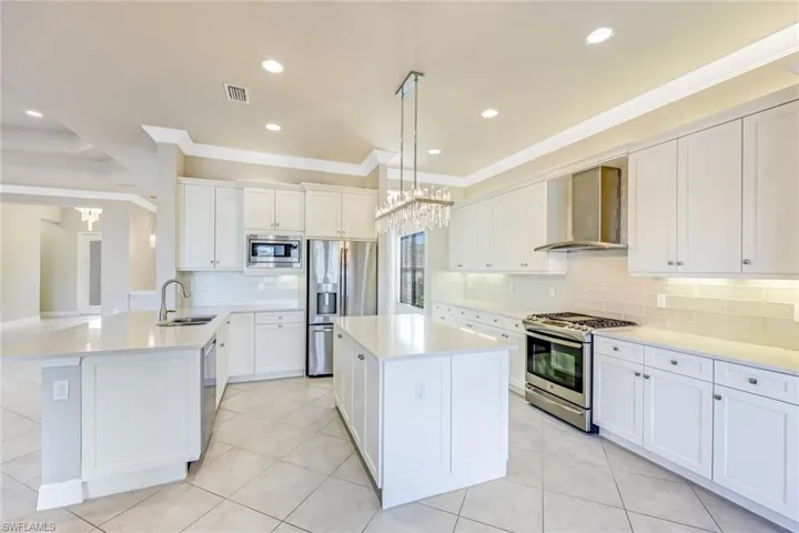 Kitchen with white cabinets, backsplash, light stone countertops, light tile patterned floors, and wall chimney exhaust hood