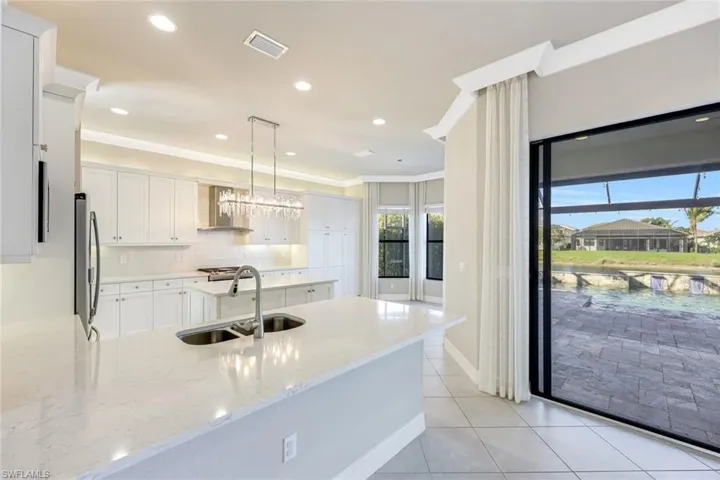 Kitchen featuring white cabinets, pendant lighting, decorative backsplash, light tile patterned floors, and wall chimney exhaust hood