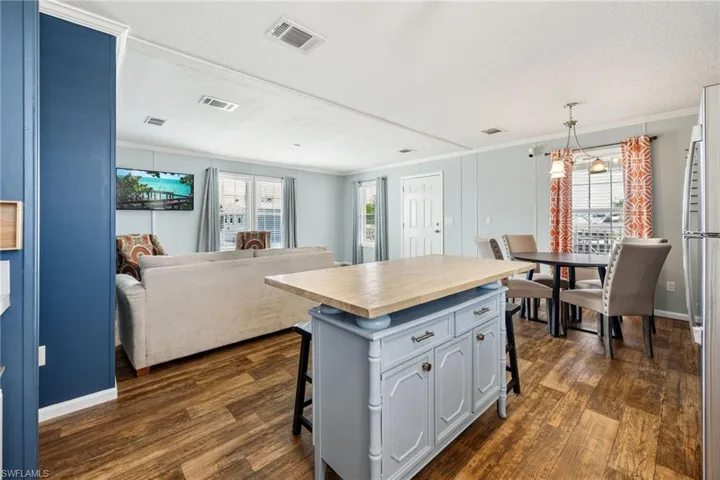 Open-concept living area featuring wood-finish flooring, a kitchen island with storage, a dining area with a chandelier, and light-colored walls.
