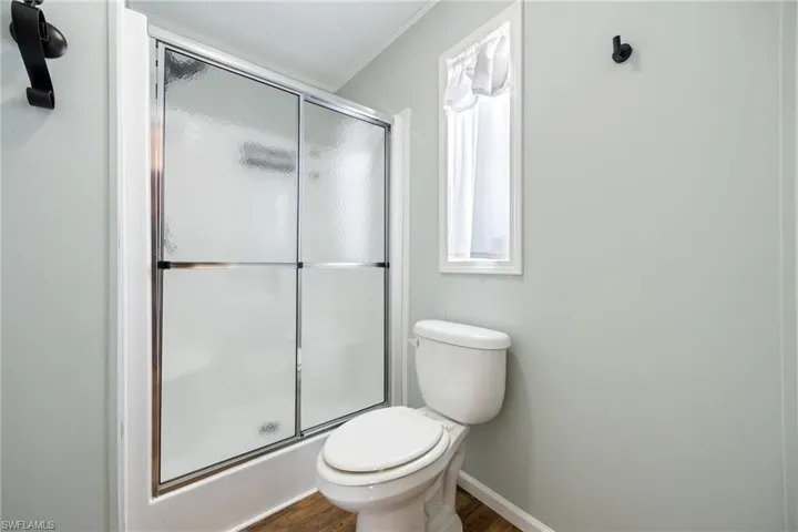 Master bathroom featuring a walk-in shower with sliding glass doors, white toilet, window with white trim, and wood-finish flooring.