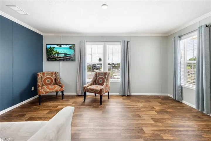 Living area featuring wood-finish vinyl flooring, white crown molding, and a prominent accent wall.