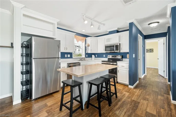 Kitchen featuring white cabinetry, wood-finish vinyl flooring, white countertops, and a center island with a wood-finish top perfect for entertaining.