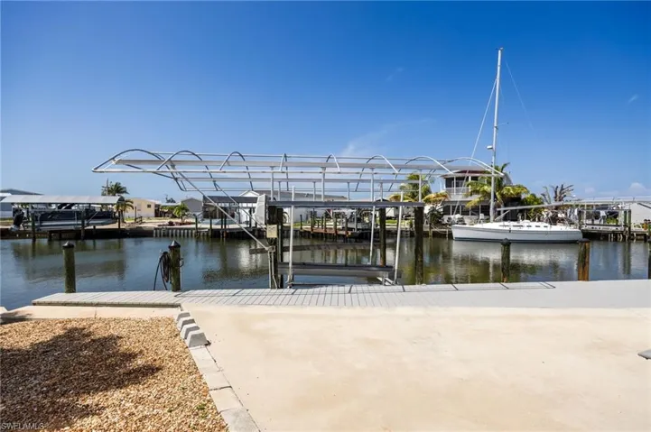 Waterfront property featuring a boat lift with canopy, composite dock, direct gulf access, and a paved concrete area.