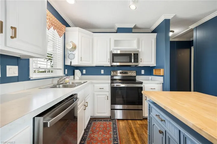 Kitchen featuring white cabinetry, stainless steel appliances, a double basin sink, light-toned countertops, and wood-finish flooring.