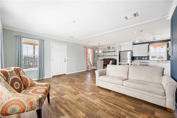 Open-concept living space featuring wood-finish flooring, a white paneled entry door, and light blue wall tones.