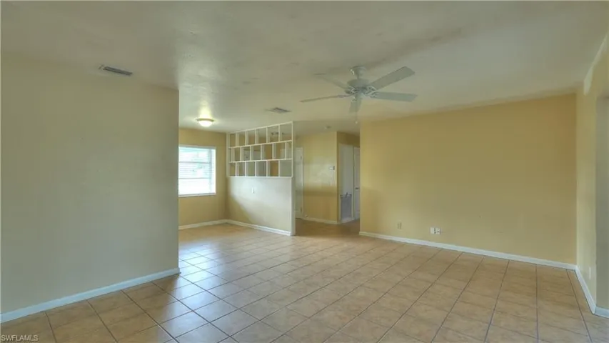 Spacious interior featuring neutral wall tones, large format tile flooring, and a ceiling fan with light fixture
