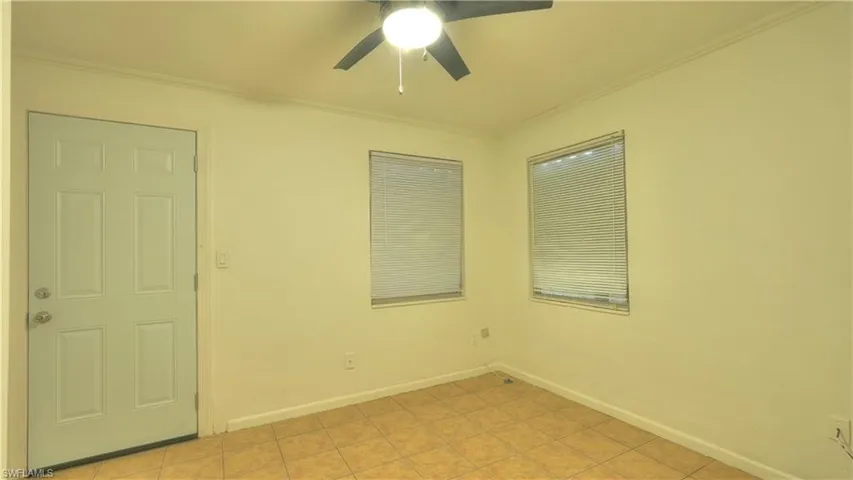 Interior room featuring light-toned walls, two windows with blinds, a white paneled door, and a ceiling fan with integrated lighting