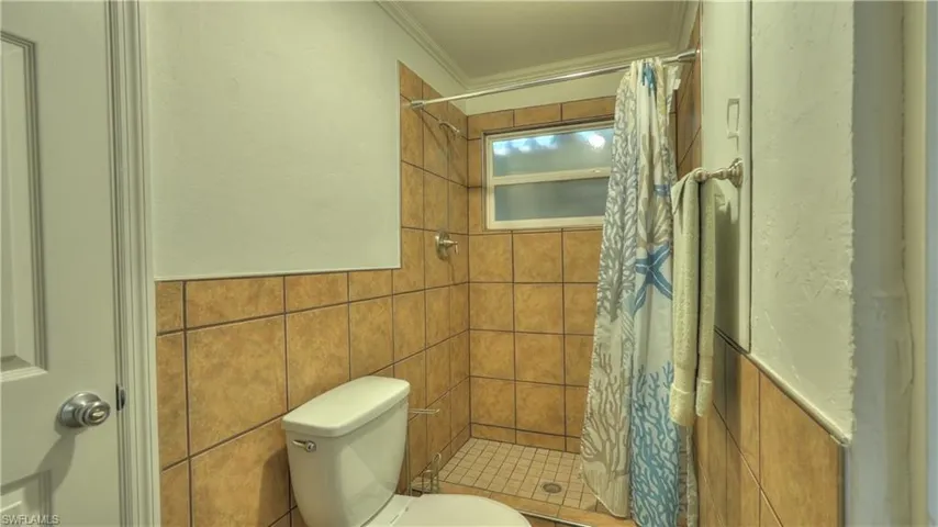Bathroom featuring a walk-in shower with full wall tiling, a window, and a white toilet