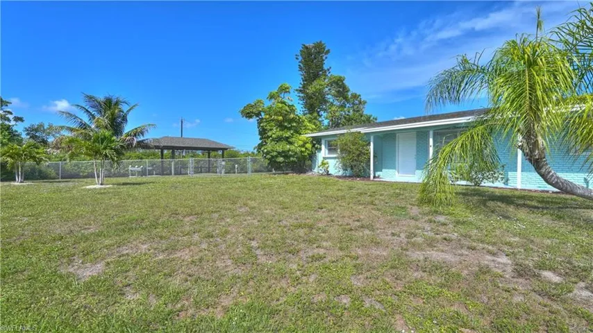 Fenced rear yard featuring a covered structure and tropical landscaping