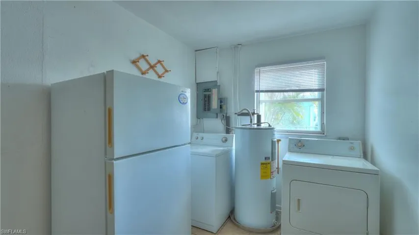 Dedicated utility space featuring a window, electrical panel, water heater, and light-colored flooring