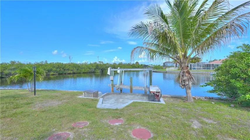 Waterfront property featuring a boat lift, concrete dock area, and mature palm trees