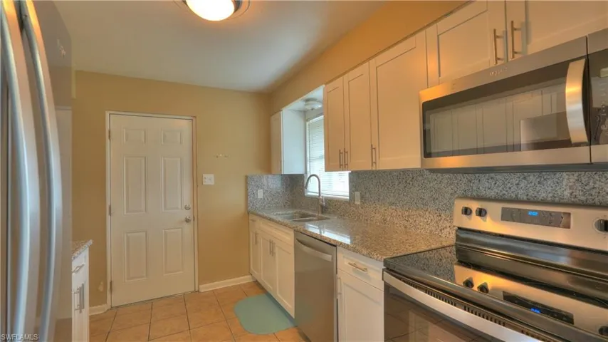 Kitchen featuring white cabinetry with brushed nickel hardware, stainless steel appliances, granite countertops, and tile flooring